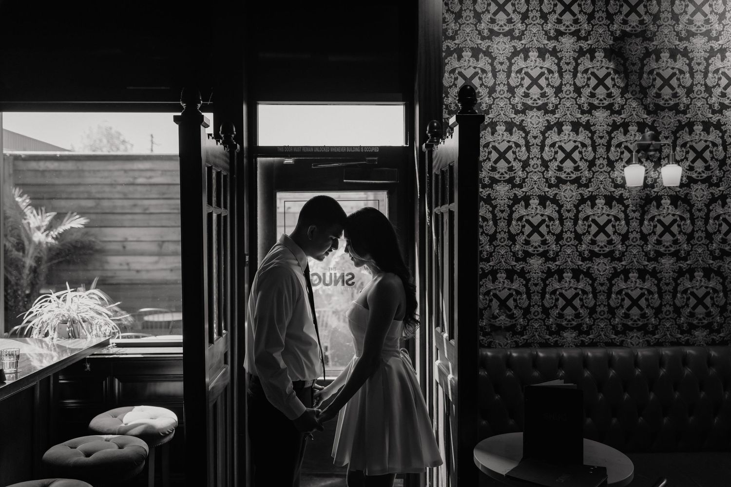 Black and white photo of a romantic couple sharing an intimate moment in a stylish interior doorway.