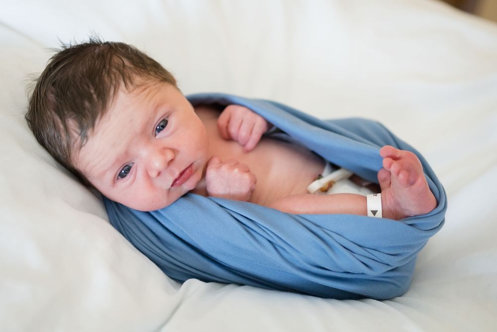 Newborn baby swaddled in a soft blue wrap, lying peacefully during a Fresh 48 Session at Fort Sanders in Knoxville, TN.