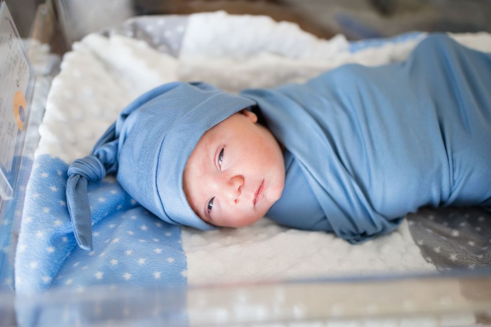 Newborn baby swaddled in blue wrap and knotted hat lying in hospital bassinet during a Fresh 48 Session at Fort Sanders in Knoxville, TN.