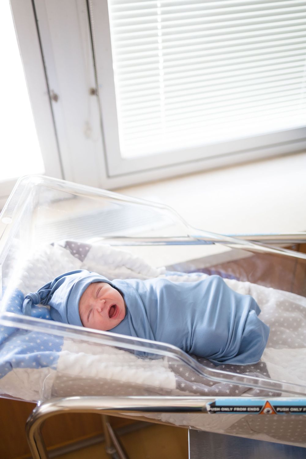 Newborn baby swaddled in blue blanket in hospital bassinet near window during a Fresh 48 Session at Fort Sanders in Knoxville, TN.