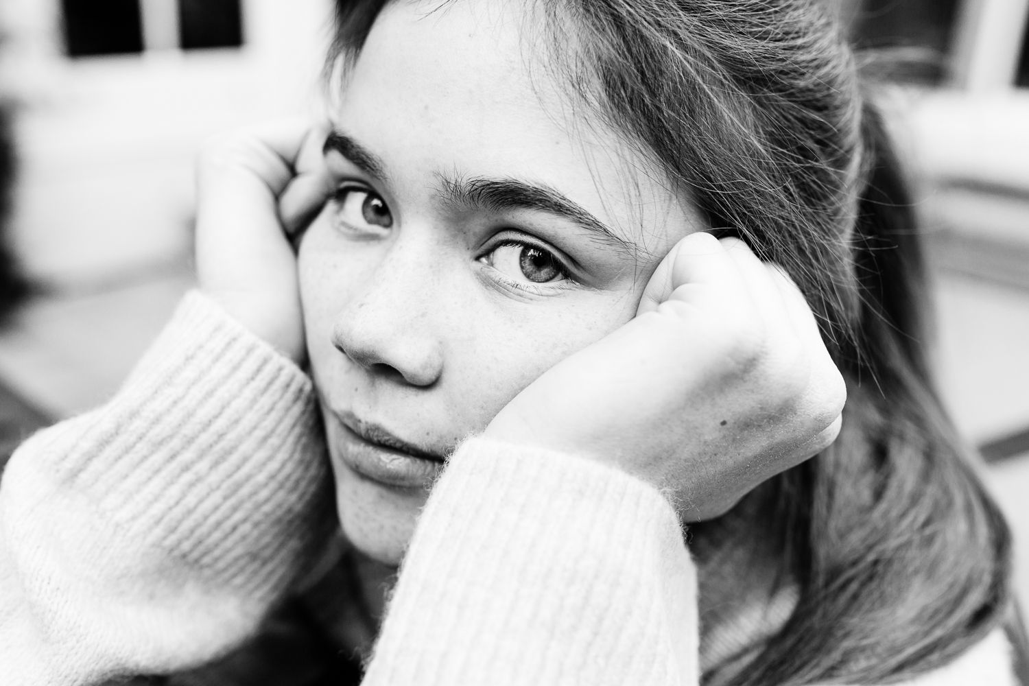 Black and white portrait of a young girl resting her face in her hands, looking thoughtful and pensive.