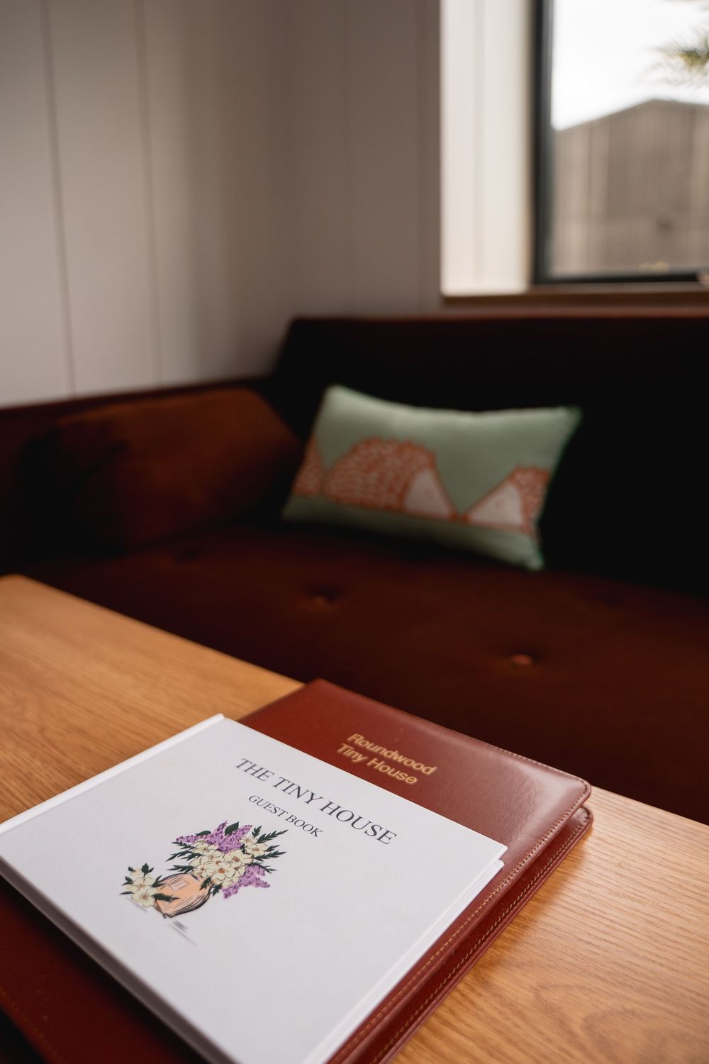 A tiny house guest book on a wooden table with a cozy brown sofa and decorative pillow in the background.