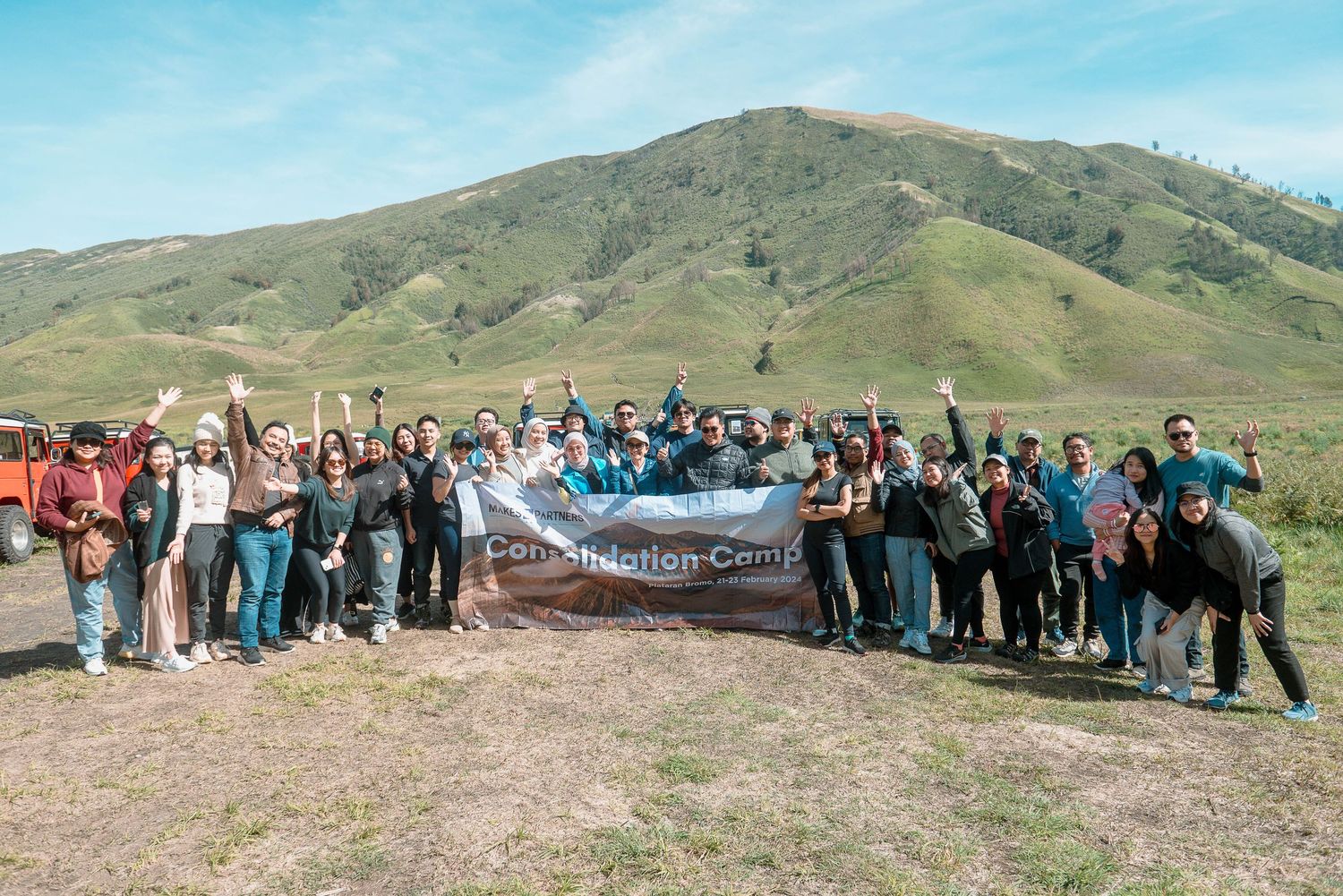 Large group of students posing with a banner outdoors at a foundation camp with green hills in background.