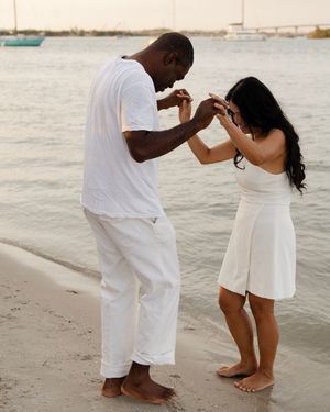 Barefoot couple holding hands on a sandy beach shore during a golden sunset.