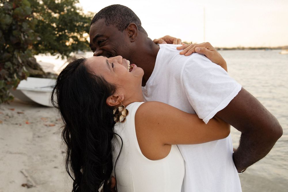 Happy couple embracing and laughing together on a sunny beach near the water.