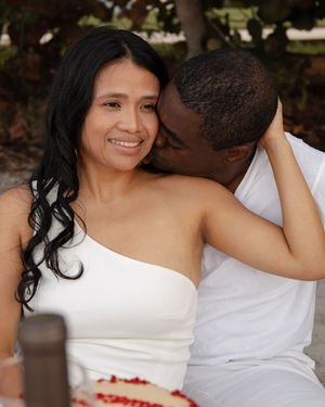 Affectionate couple sharing a quiet moment together outdoors, man kissing woman's cheek near red cake.