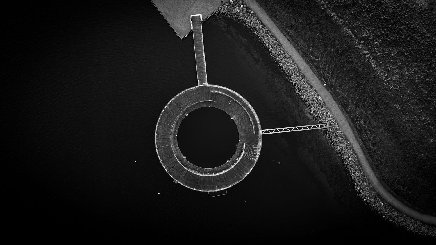 Sort-hvidt dronefotografi af rund konstruktion ved vandet – minimalistisk fotokunst og grafisk plakat til hjemmet.