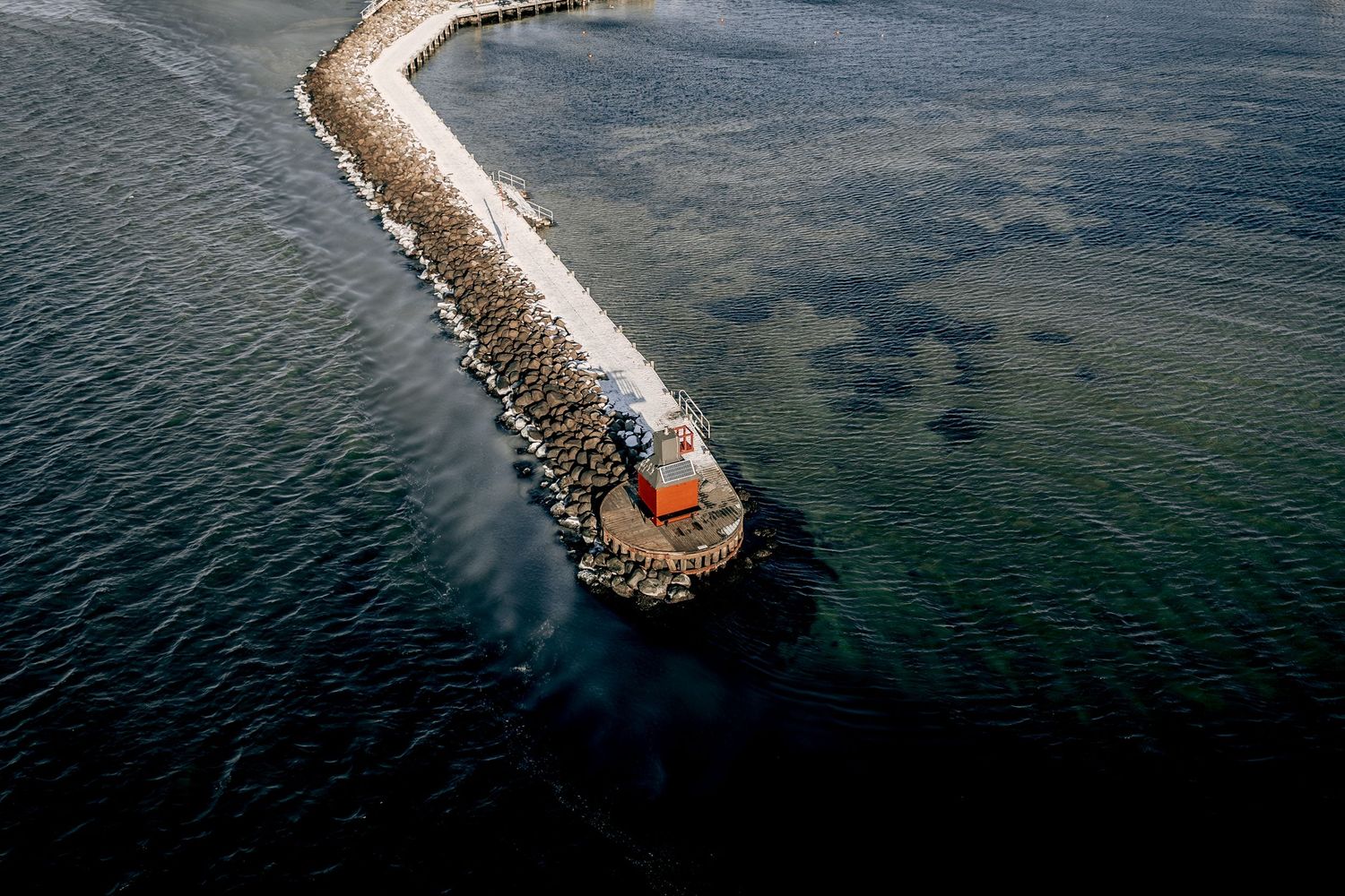 Dronefotografi af fyrtårn for enden af lang mole – maritim fotokunst og kystplakat til hjemmet.