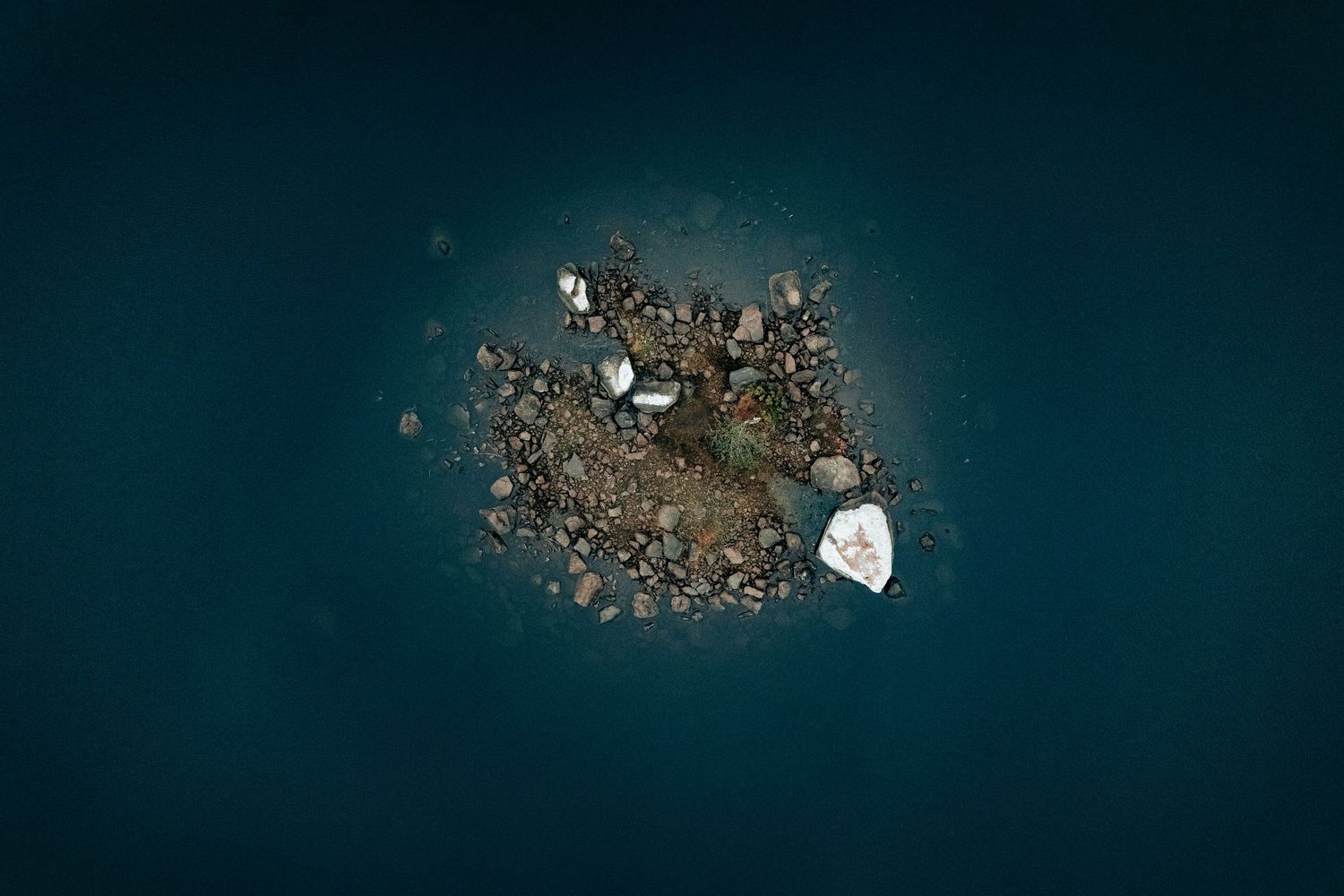 Dronefotografi af lille klippeø omgivet af mørkt vand – minimalistisk naturfotografi som fotokunst og kunstprint.