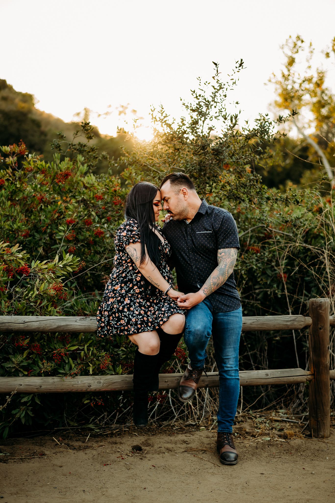 Couple sharing a romantic moment on a rustic fence at golden hour, surrounded by lush greenery.