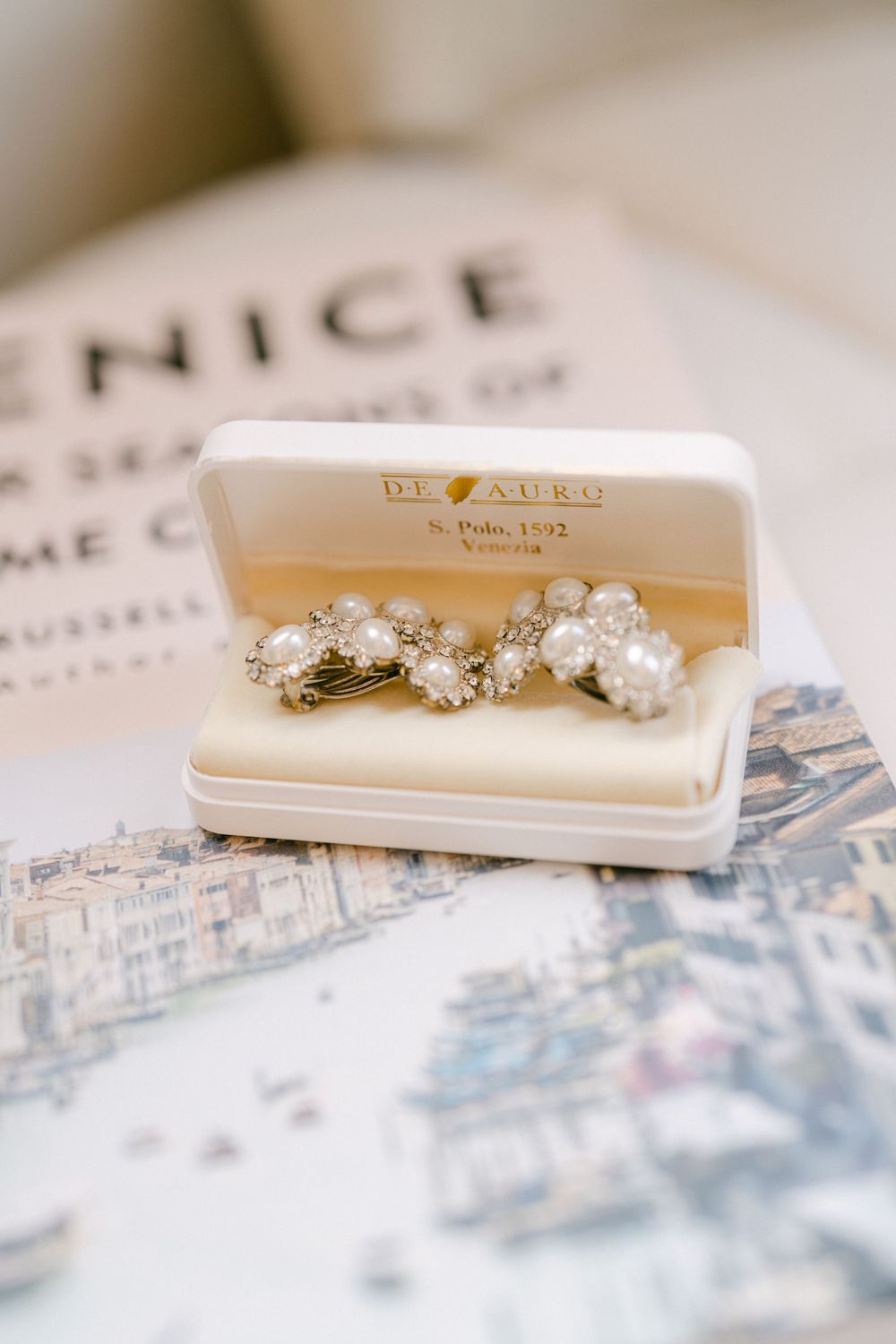 Vintage pearl earrings displayed in an antique jewelry box on a patterned surface.