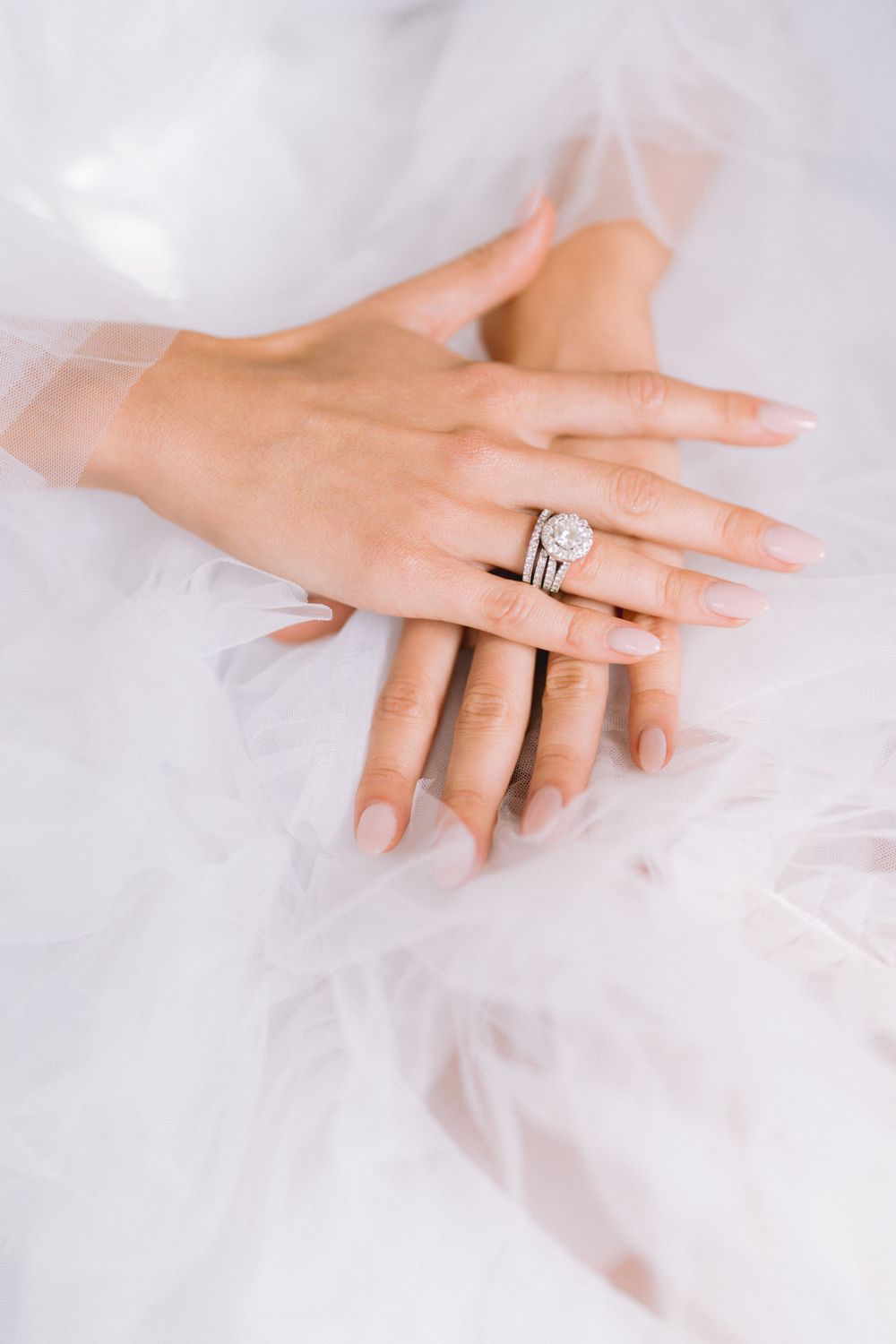 Close-up shots of an elegant engagement ring on a bride's hand against white tulle fabric.