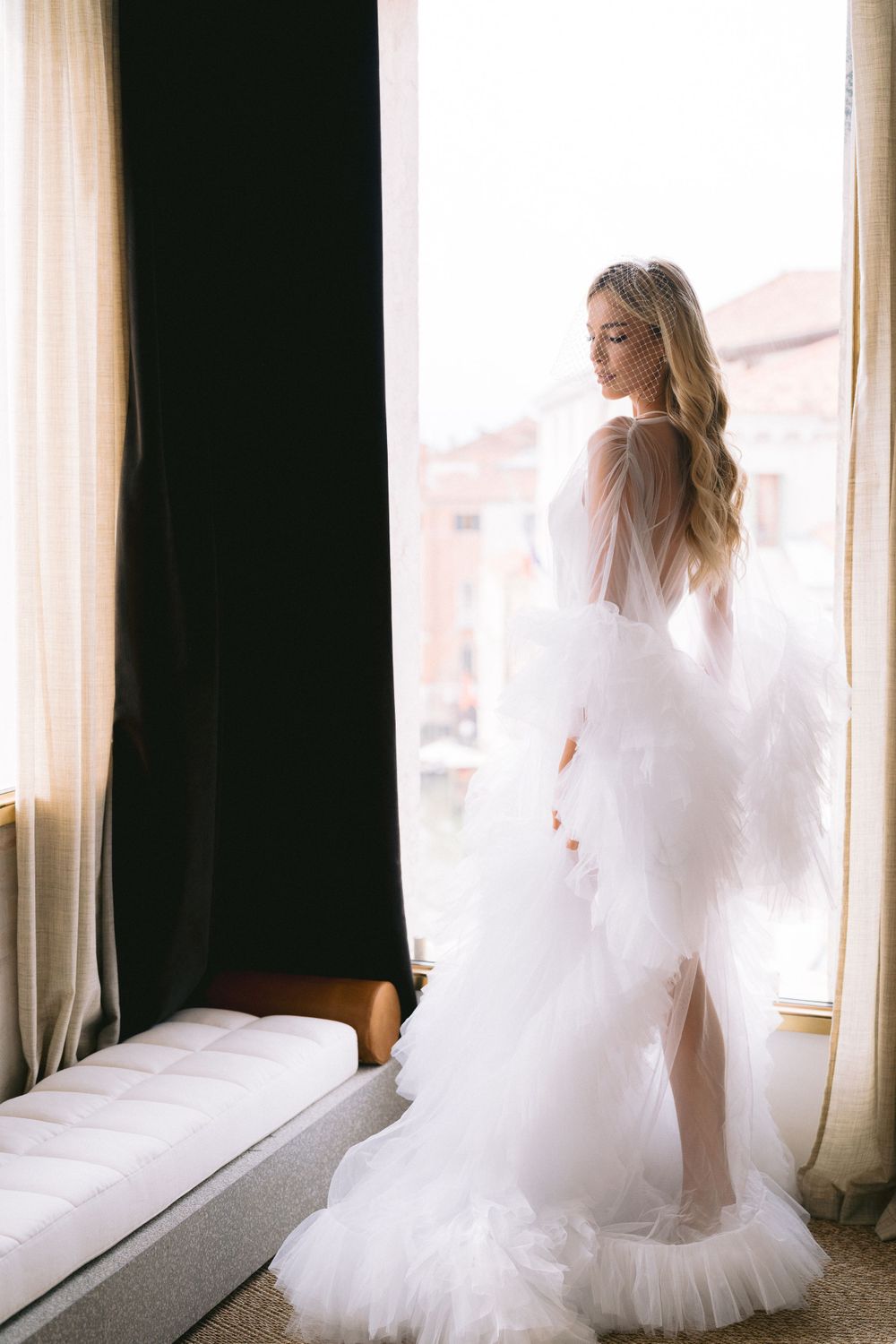 Ethereal bridal portraits by a window showing the flowing movement of a white wedding dress.