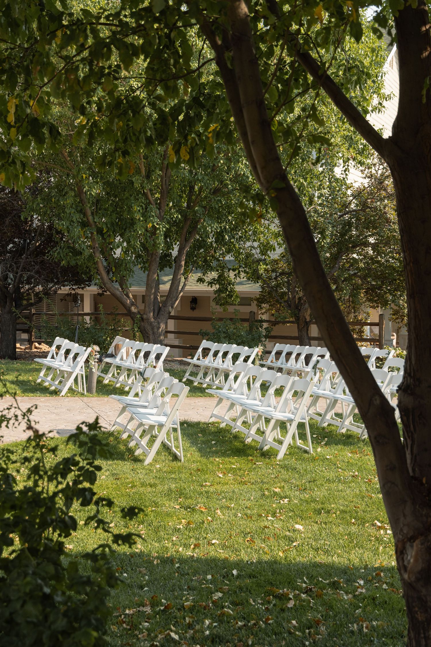 A bride in a lace gown and veil holds hands with a groom in a black tuxedo walking through an outdoor garden venue.