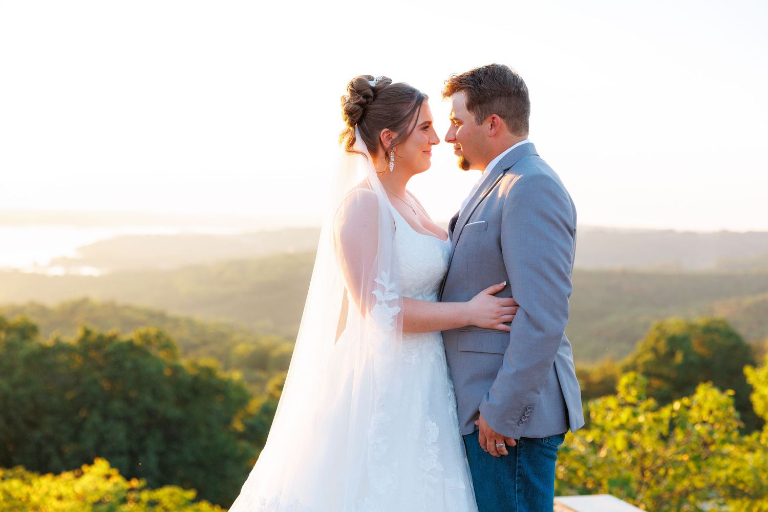 Bride and groom share a romantic moment at sunset overlooking lush green hills on their wedding day.