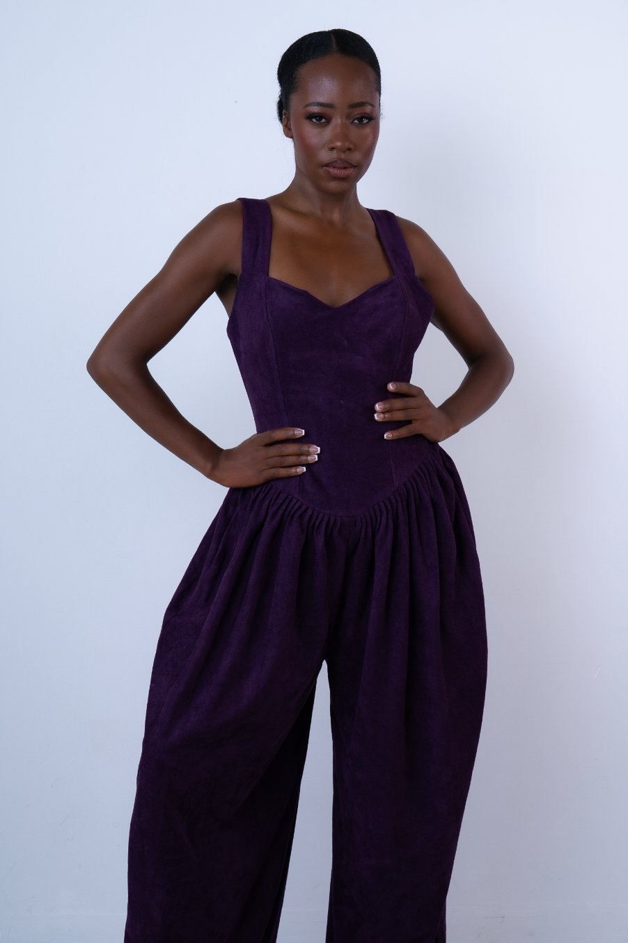 Woman wearing a deep purple sleeveless jumpsuit with sweetheart neckline and wide-leg trousers, posing confidently.