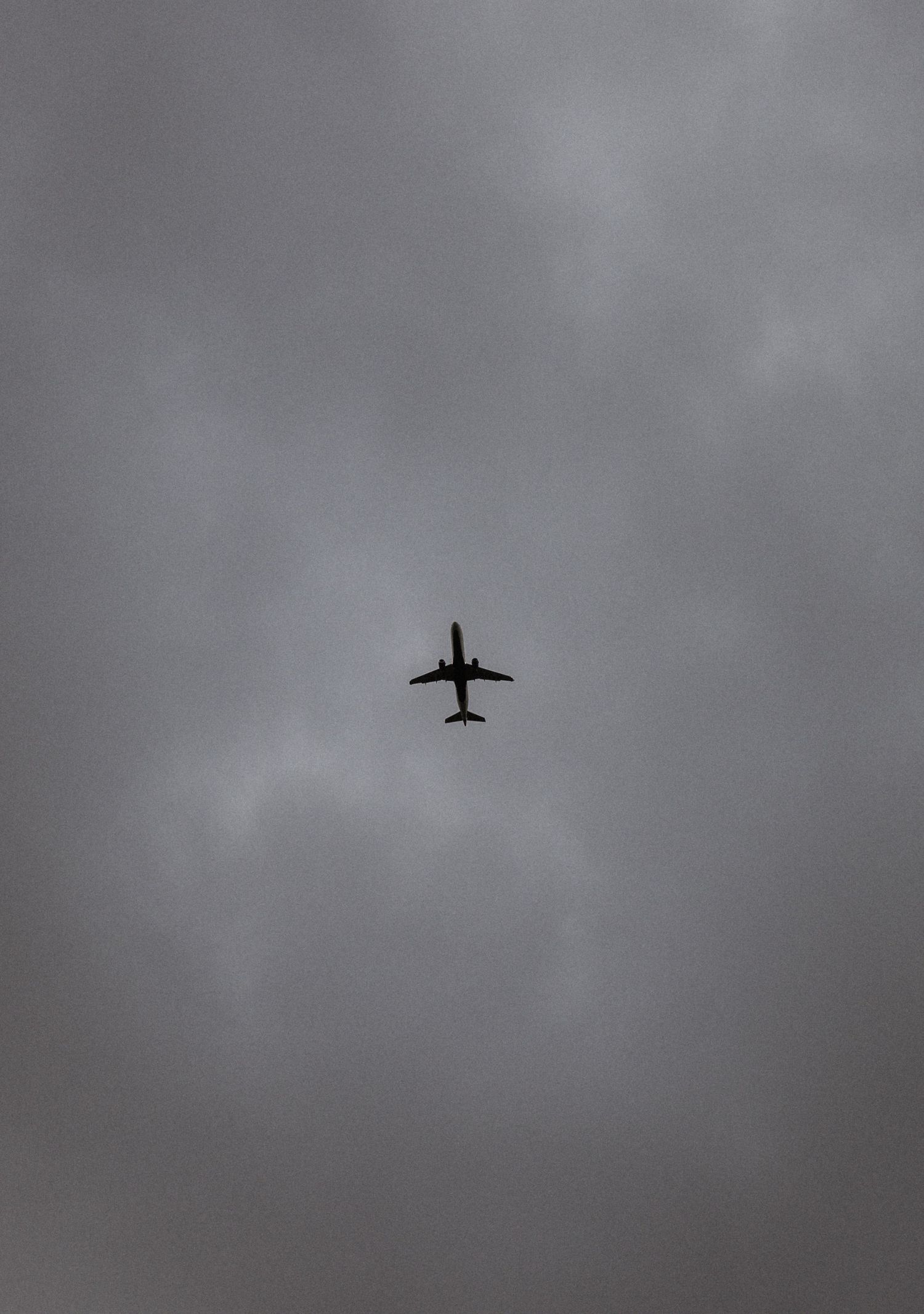 Silhouette of a commercial airplane flying through overcast gray cloudy sky, viewed from below.