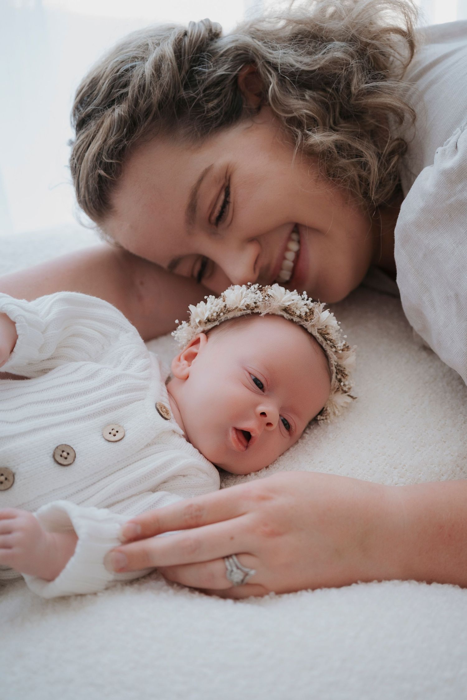Two newborn twins lying side by side on a knit blanket, wearing neutral-toned outfits with hospital ID bracelets.