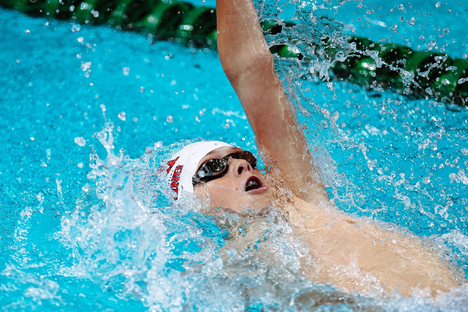 Swimmer celebrating in pool at Hancock Prospecting event, wearing red cap, with Swiss Timing scoreboard visible.