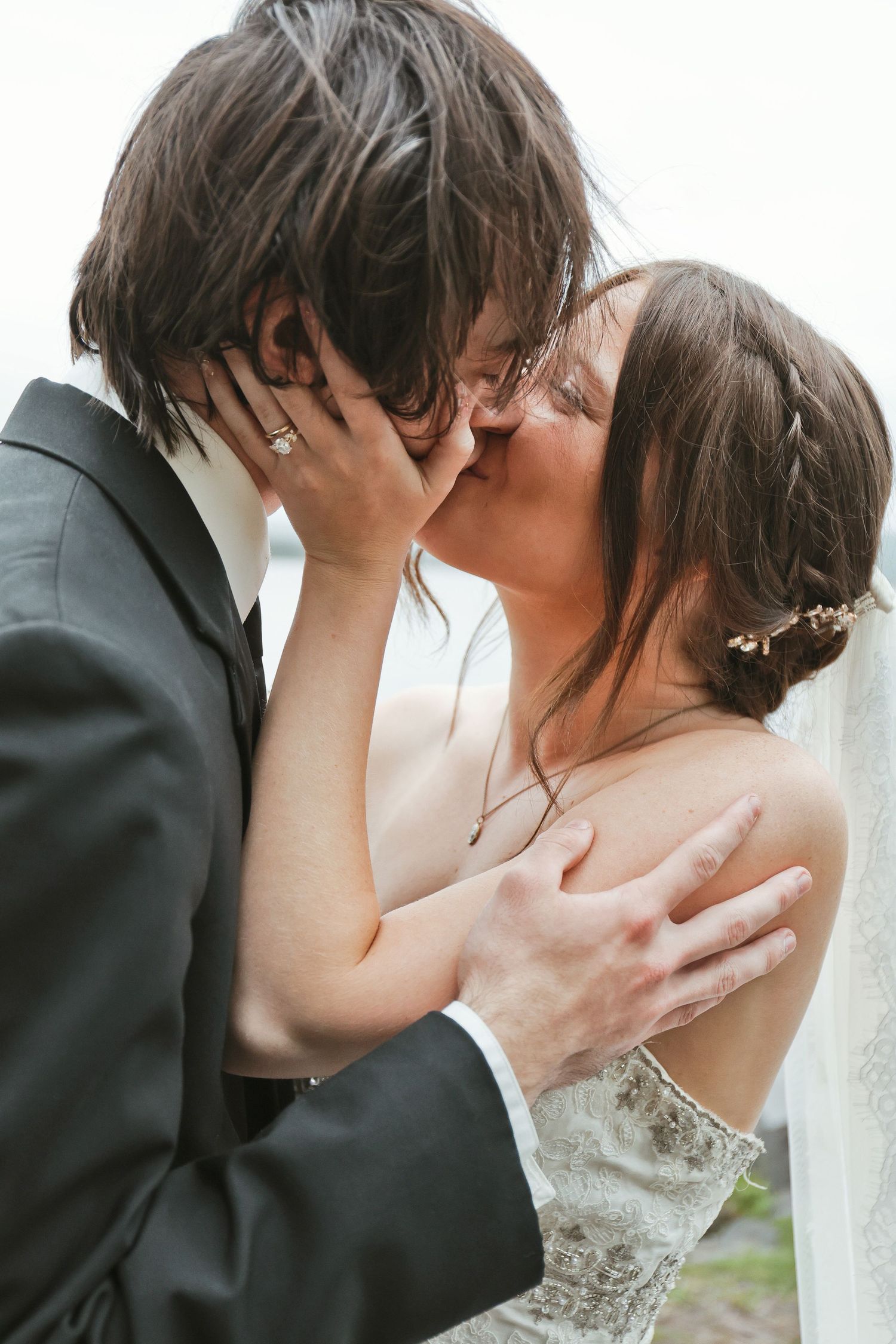 A bride and groom share a romantic kiss on their wedding day, with the bride in lace and a floral hair piece.
