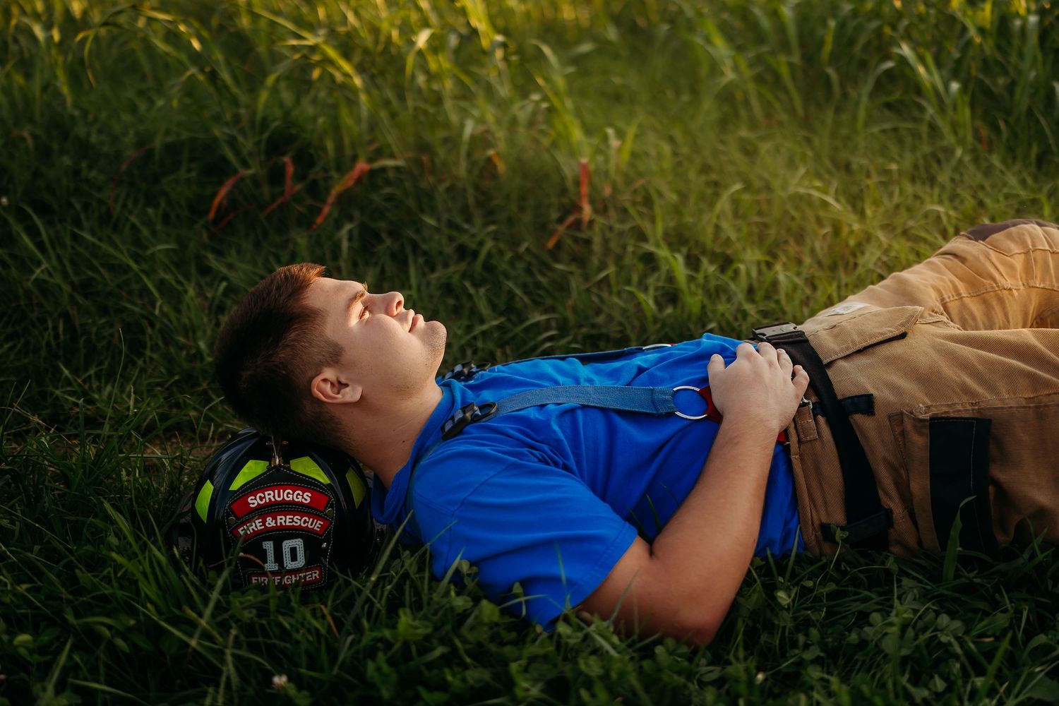 A young boy in a blue shirt rests on green grass beside a soccer ball in warm golden sunlight.