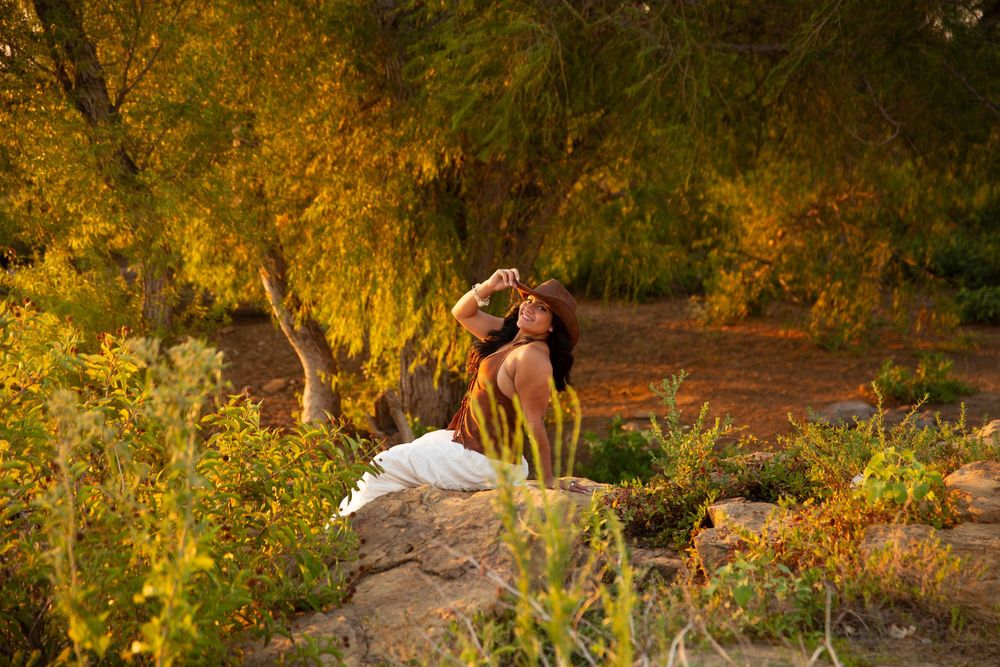 Couple embracing romantically outdoors among lush golden trees and desert plants at sunset.