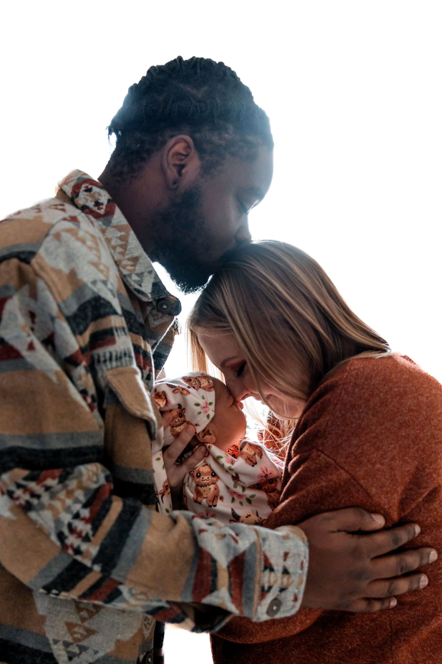 Interracial couple sharing tender moment, cradling newborn baby together in warm autumn clothing.