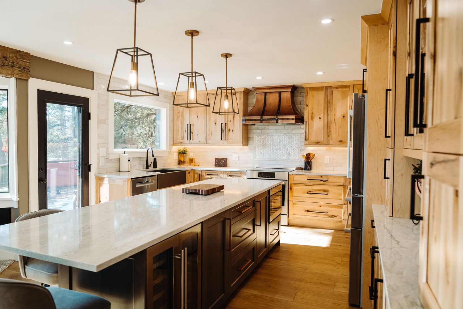 Modern farmhouse kitchen with light wood cabinets, dark island, quartz countertops, pendant lights, and herringbone tile backsplash.