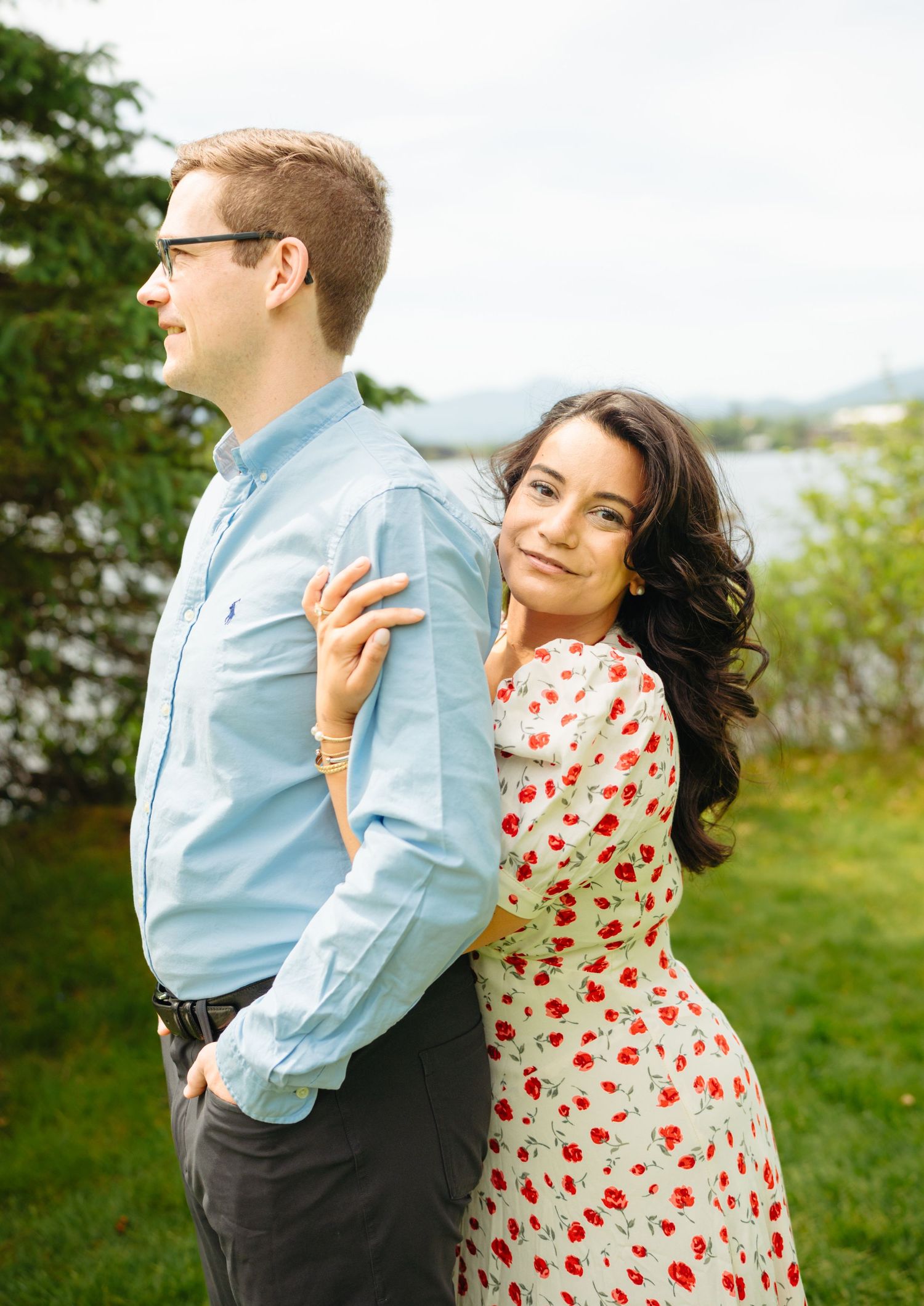 Couple posing back to back outdoors, woman in red floral dress smiling over her shoulder.