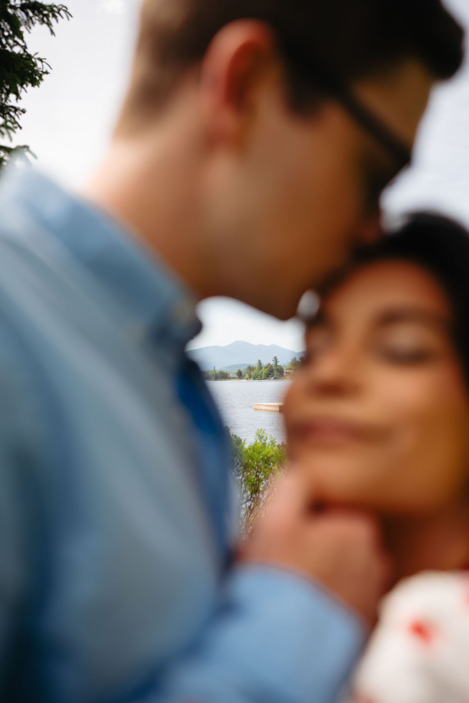Romantic couple sharing an intimate moment near a serene lake with mountain views in the soft-focus background.