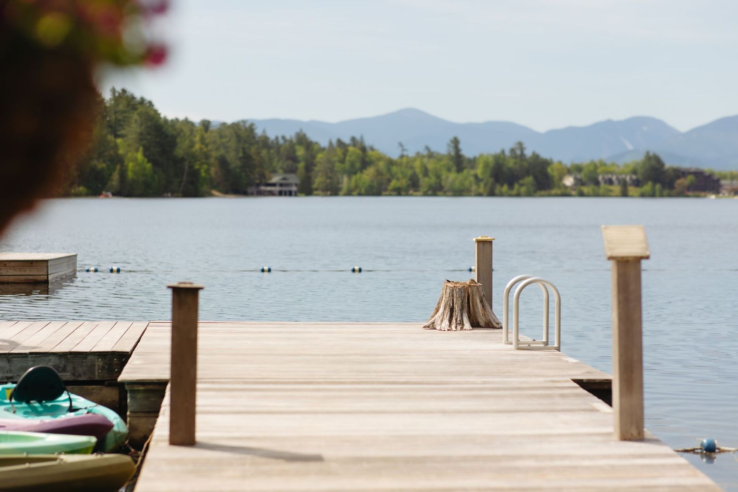 Wooden dock extending over a calm lake with mountain views, ladder, and kayak on sunny day.