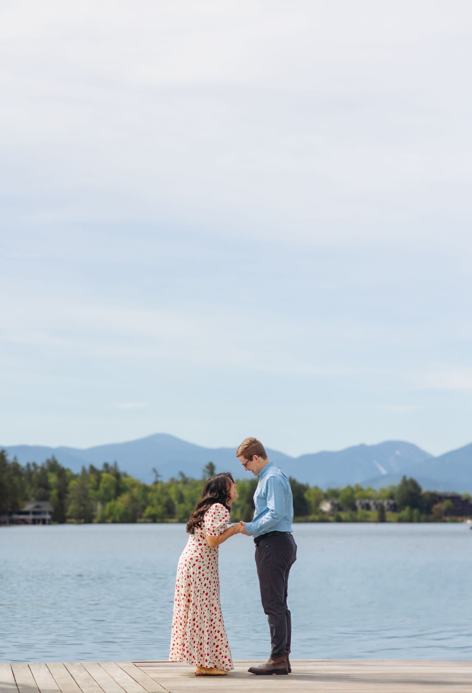 Couple holding hands on a dock with mountain lake views in the background.