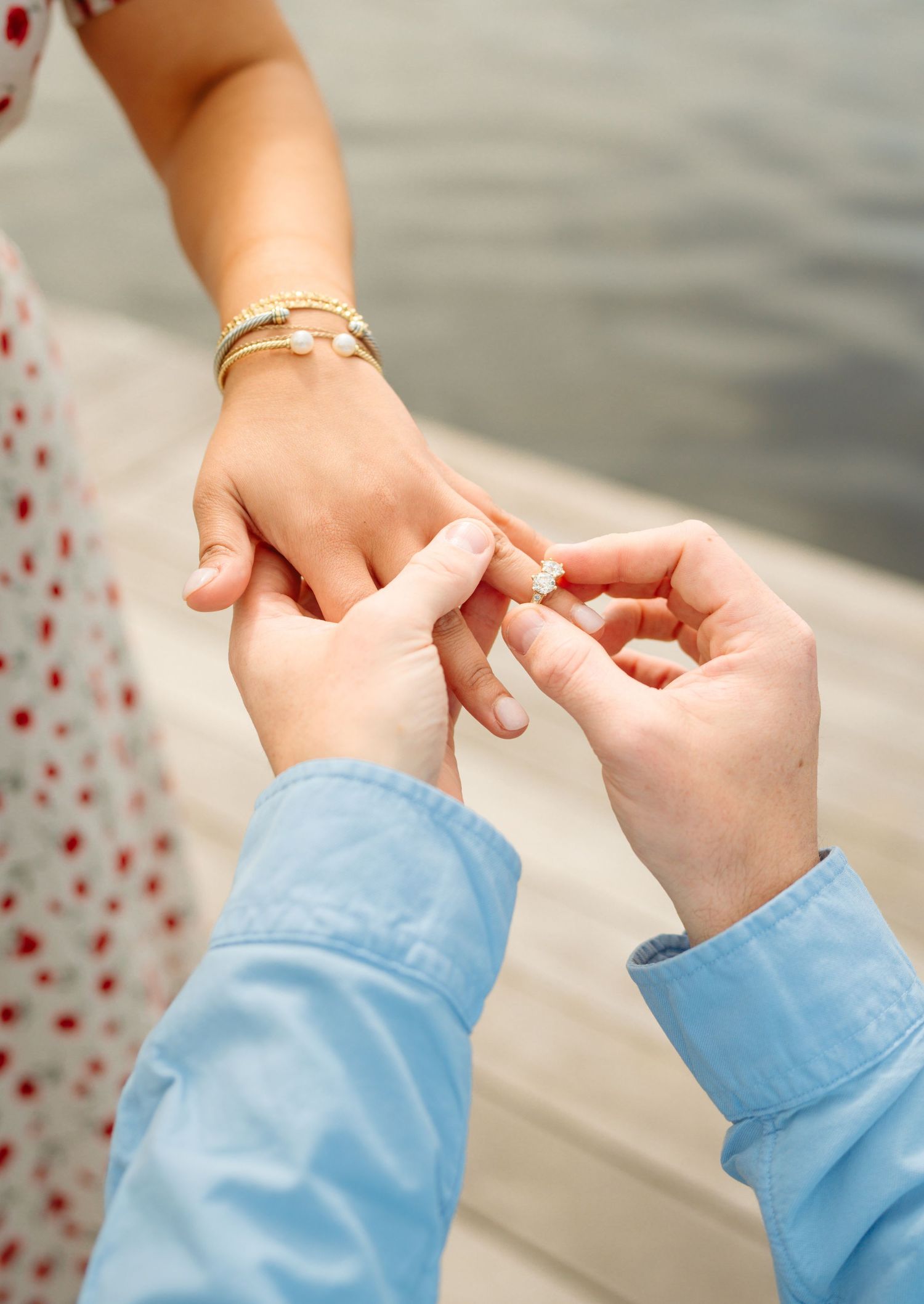 Man placing engagement ring on woman's finger near waterfront, romantic proposal moment.