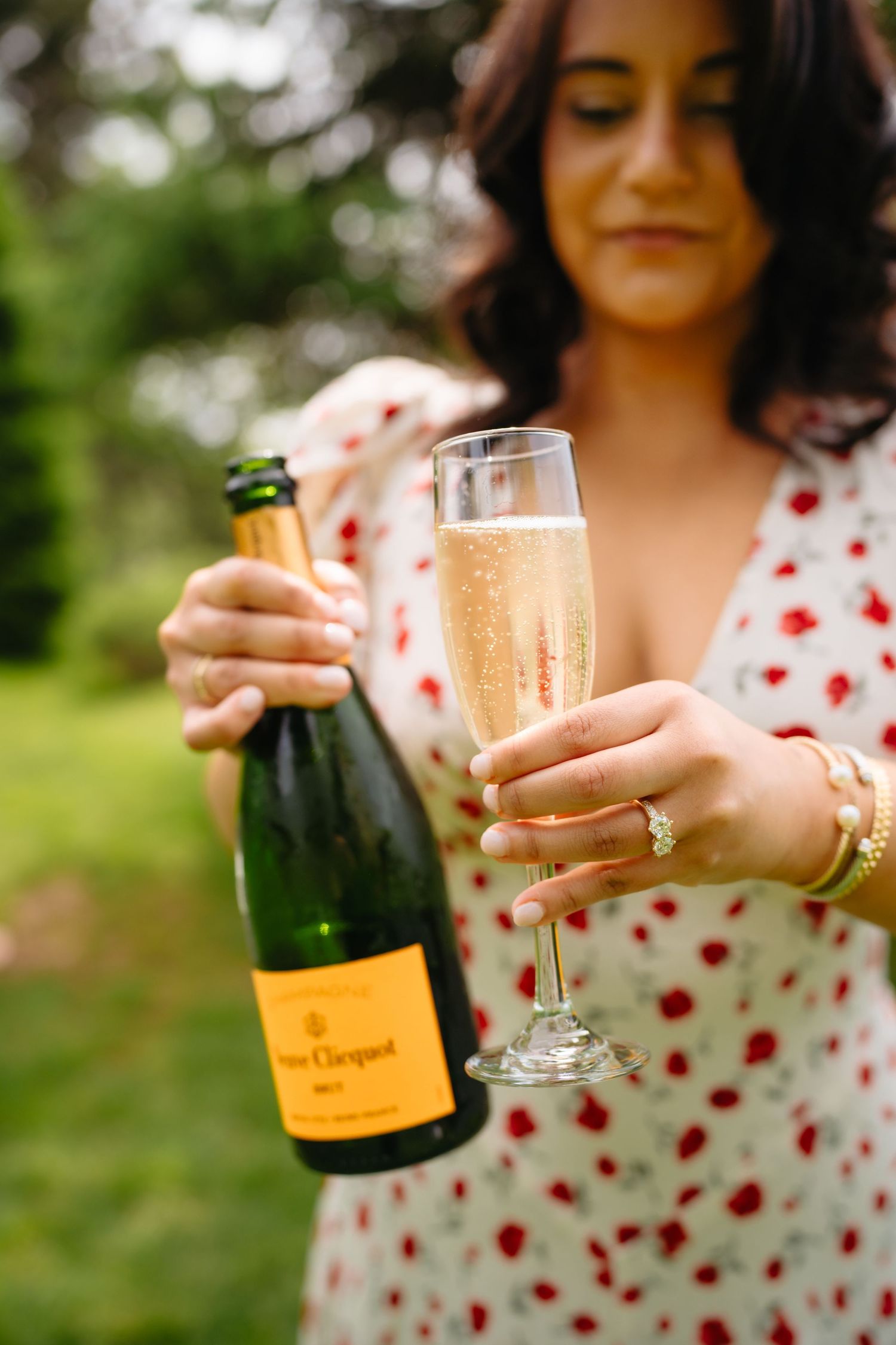 Woman in floral dress holding Veuve Clicquot champagne bottle and flute outdoors.