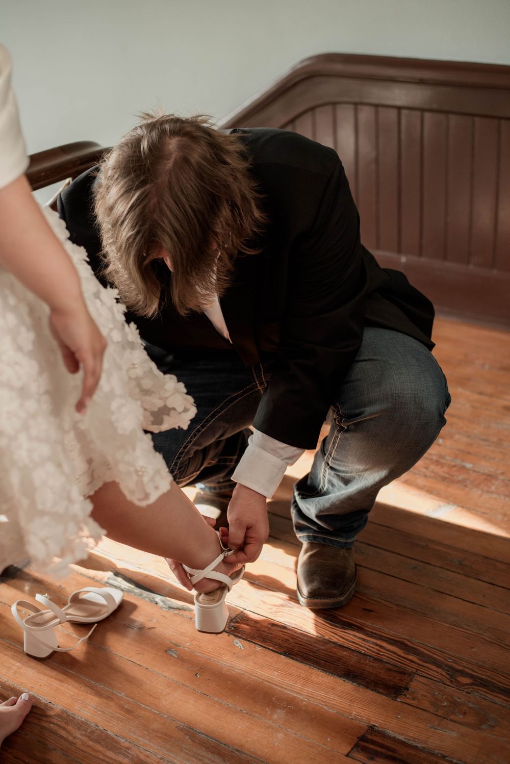 Groom kneels to help the bride with her wedding shoes inside the Weatherford Courthouse before their ceremony.
