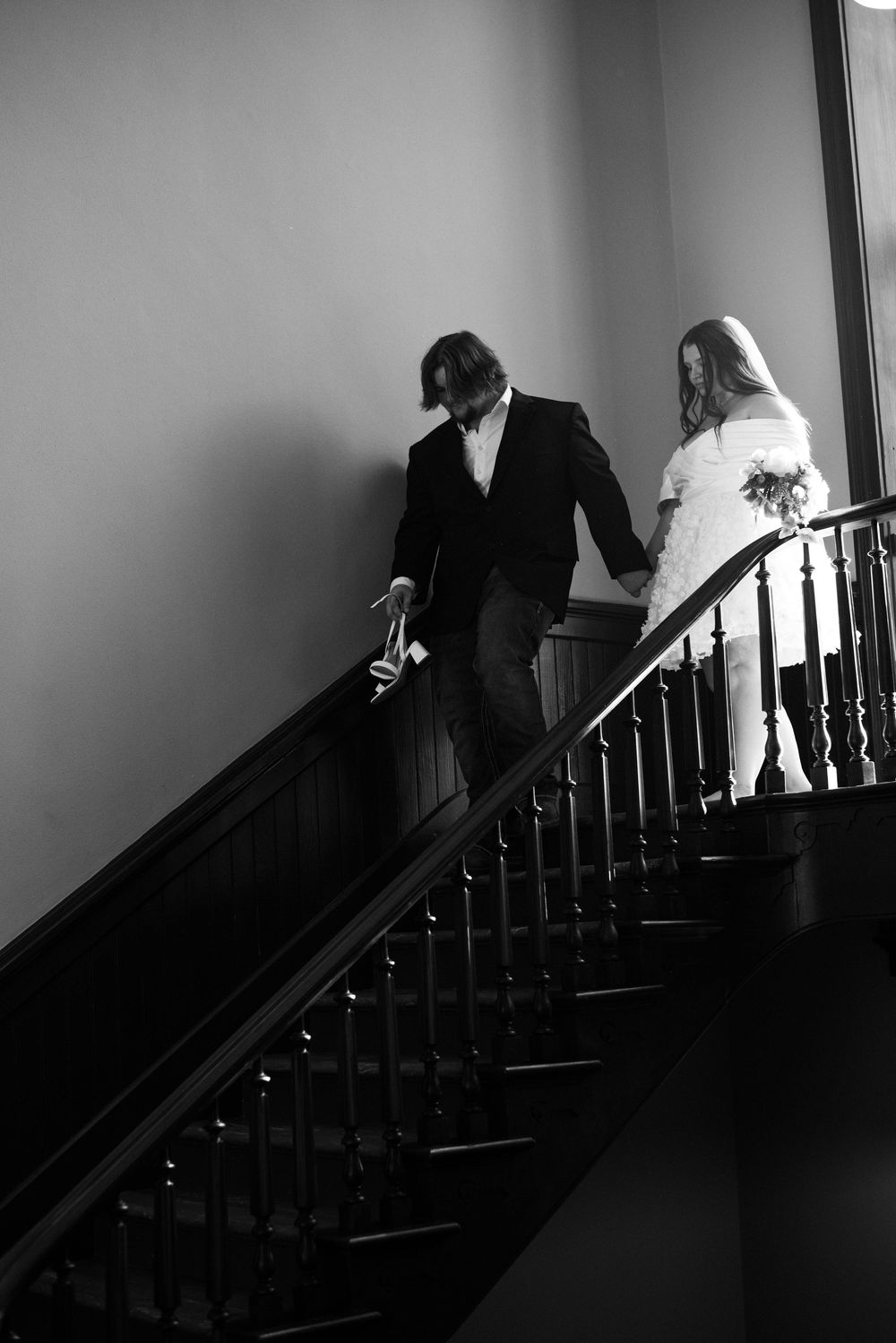Black-and-white photograph of newlyweds holding hands as they walk down the staircase inside the Weatherford Courthouse.