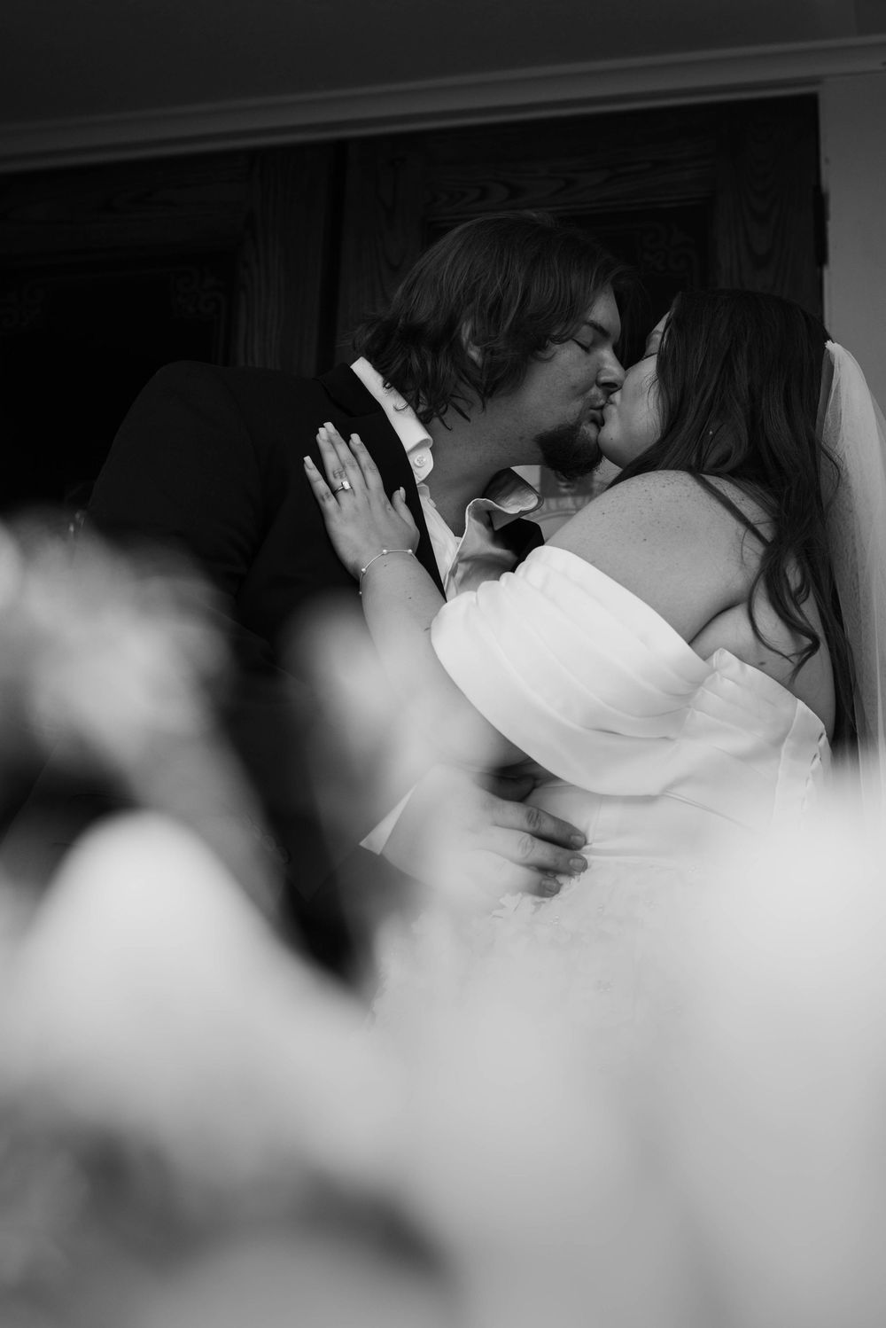 Black-and-white photograph of newlyweds sharing their first kiss as guests celebrate inside the Weatherford Courthouse.