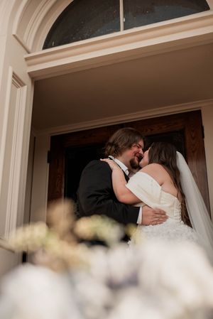 Newlyweds kiss in the Weatherford Courthouse doorway beside white floral arrangements after their ceremony.