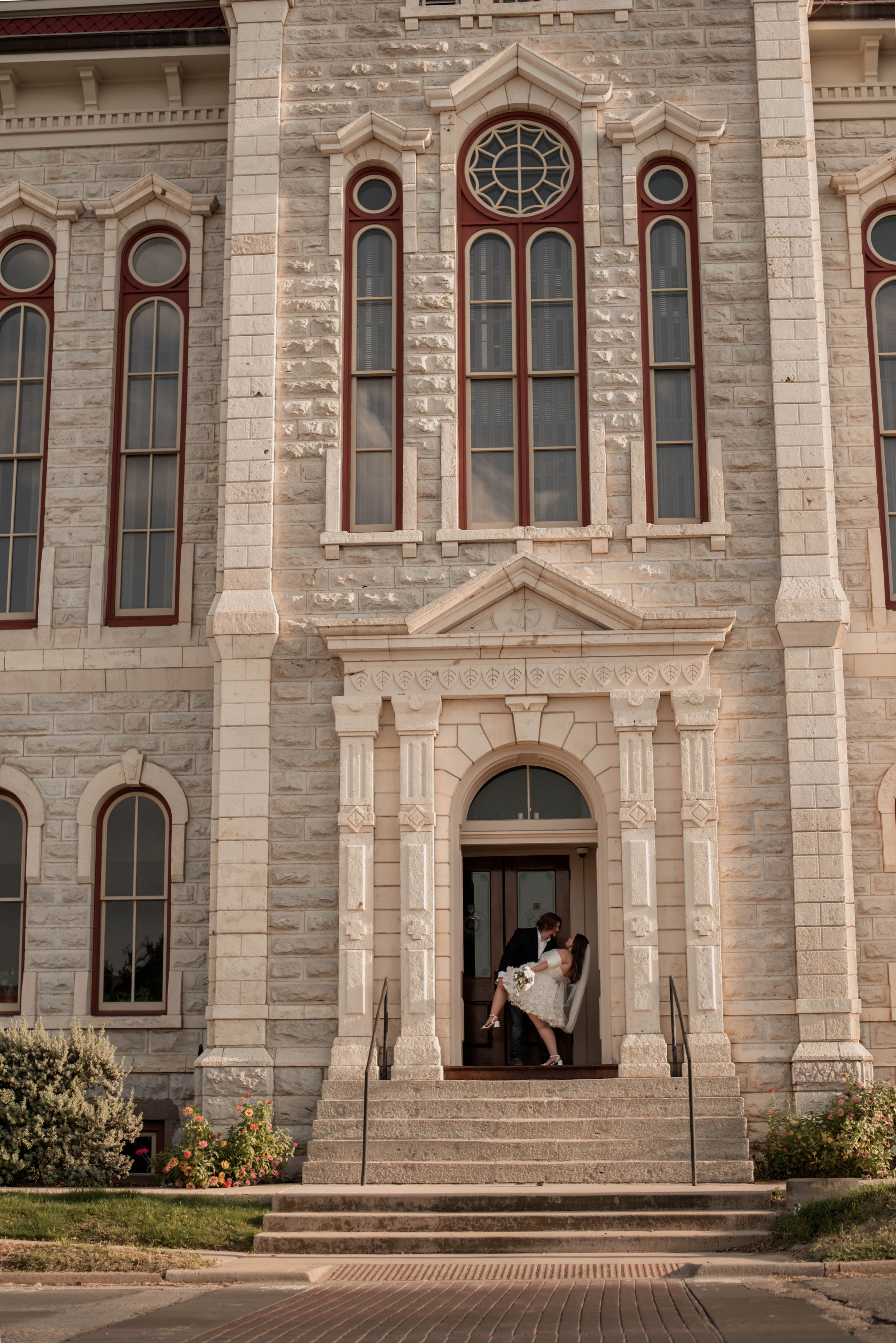Newlyweds kiss in an arched doorway outside the historic Weatherford Courthouse after their wedding ceremony.