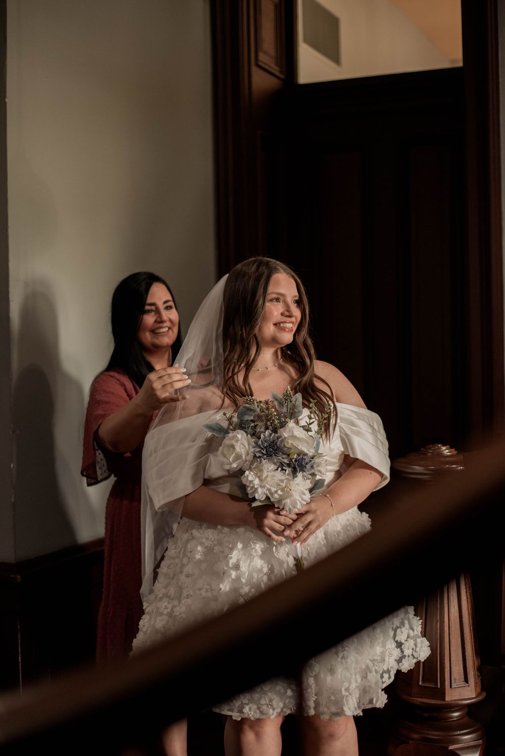 Bride smiles as a bridesmaid adjusts her veil before her wedding ceremony inside the Weatherford Courthouse.