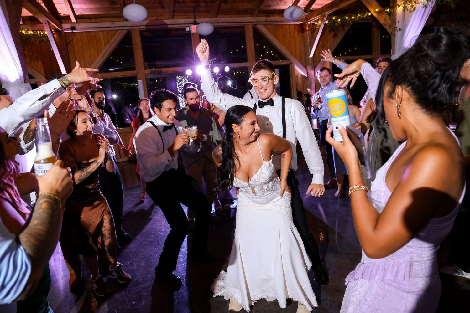 Bride and groom share joyful first dance surrounded by cheering wedding guests in a warmly lit rustic venue.