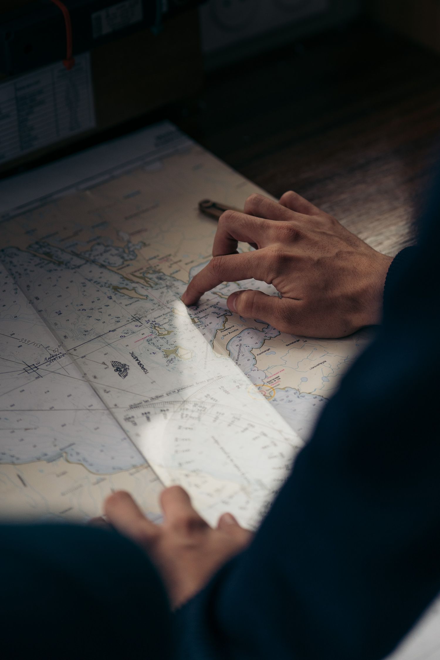 Mains traçant une route sur la carte marine du Polarfront en lumière rasante