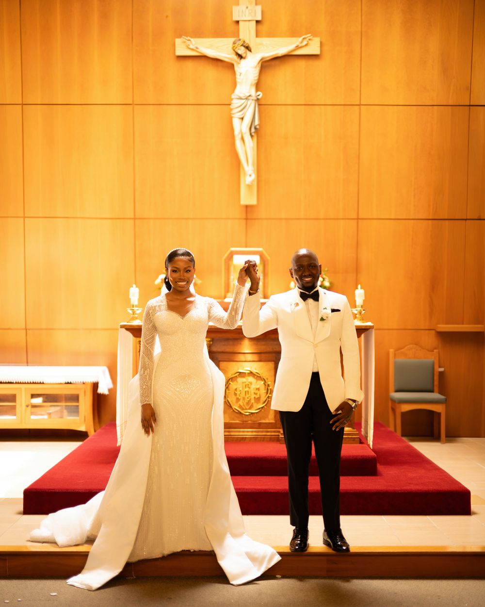 Bride and groom celebrate at church altar beneath crucifix in classic white wedding attire.