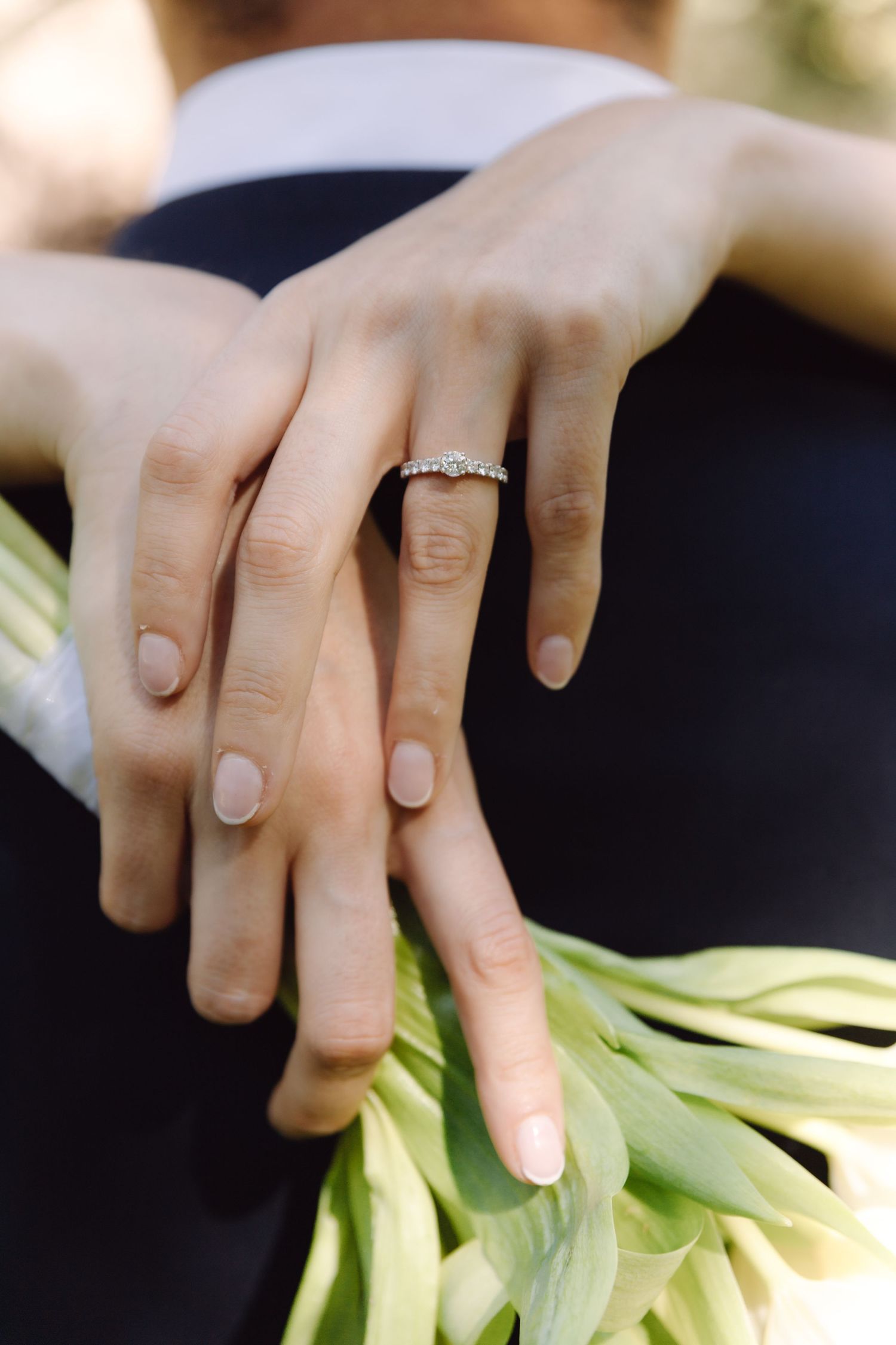 Close-up of bride\u2019s hands showing diamond engagement ring as she embraces groom holding white tulips.