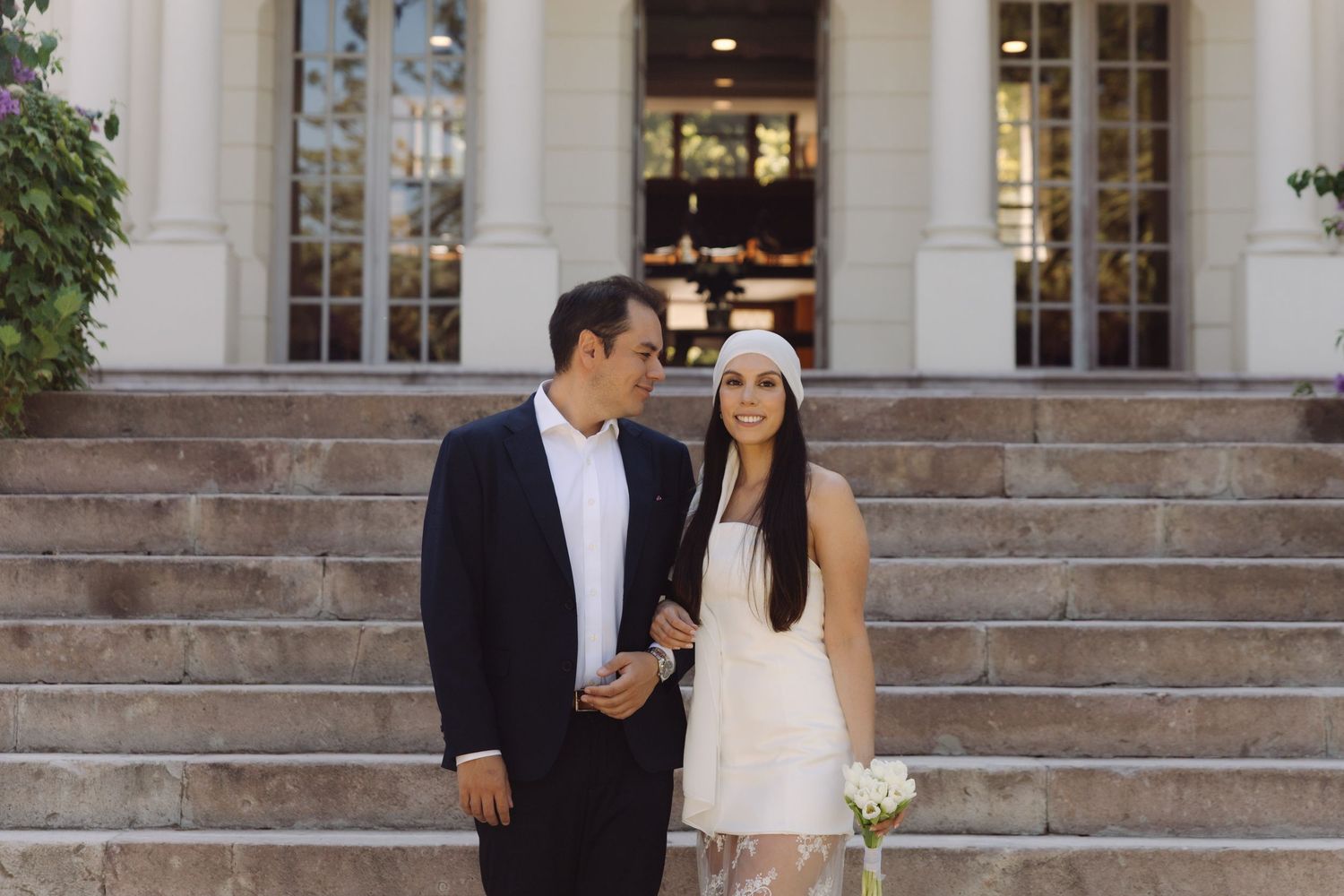 Wedding couple sharing an intimate moment on stone steps outside a classic white building.