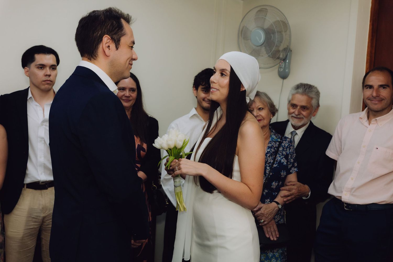Bride and groom sharing a tender moment during indoor wedding ceremony, bride holding white floral bouquet.