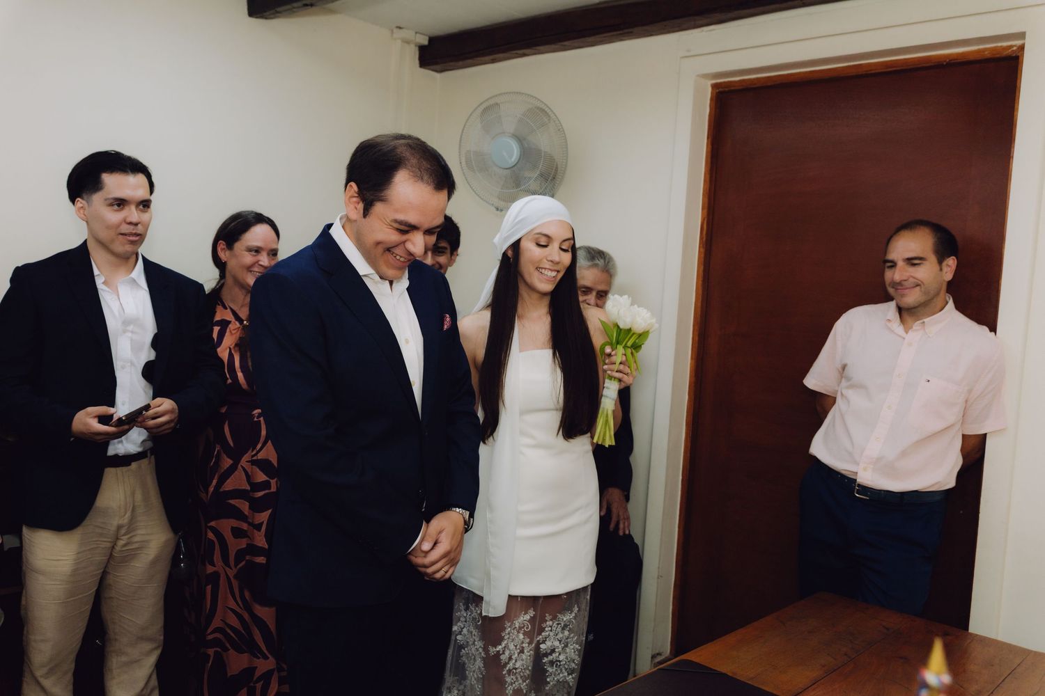 Bride holding white tulips walks with groom during indoor civil wedding ceremony.