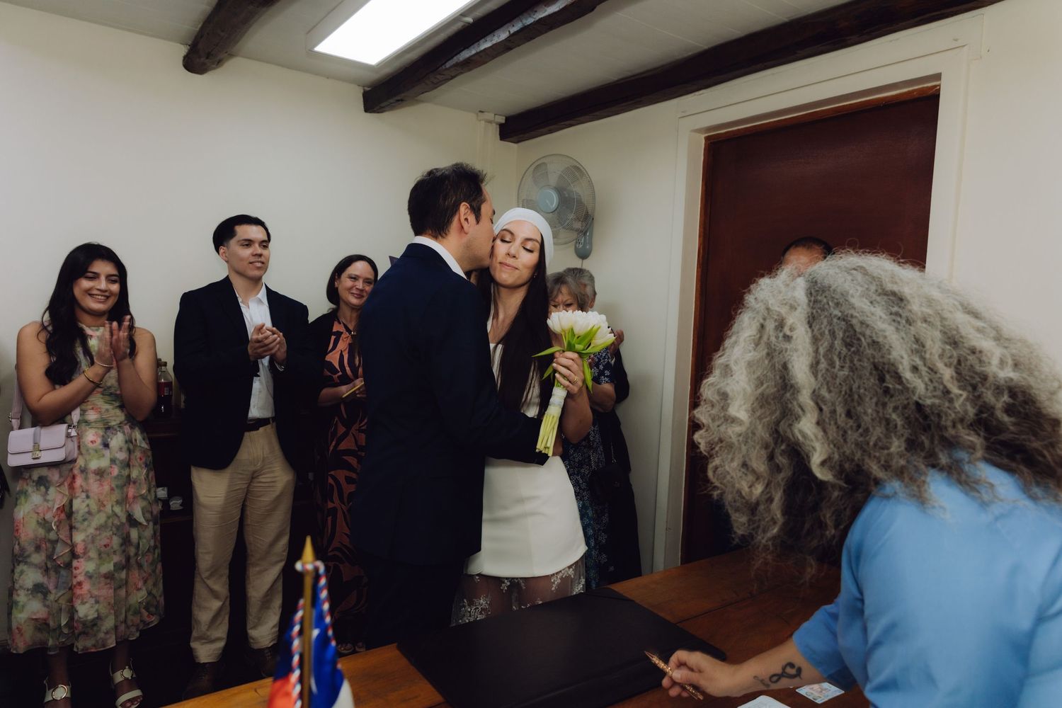 Groom kisses bride as guests applaud at the conclusion of civil wedding ceremony.