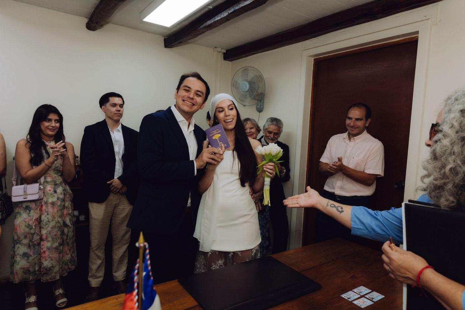 Newlyweds pose together smiling with guests clapping after civil wedding ceremony.