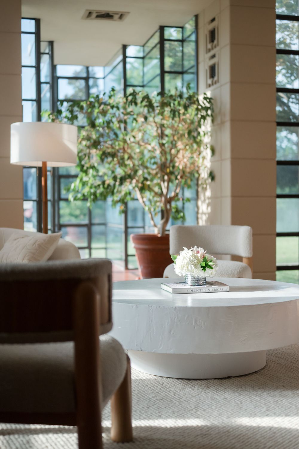 Modern living room interior with white round coffee table, potted plants and large windows bringing in natural light.